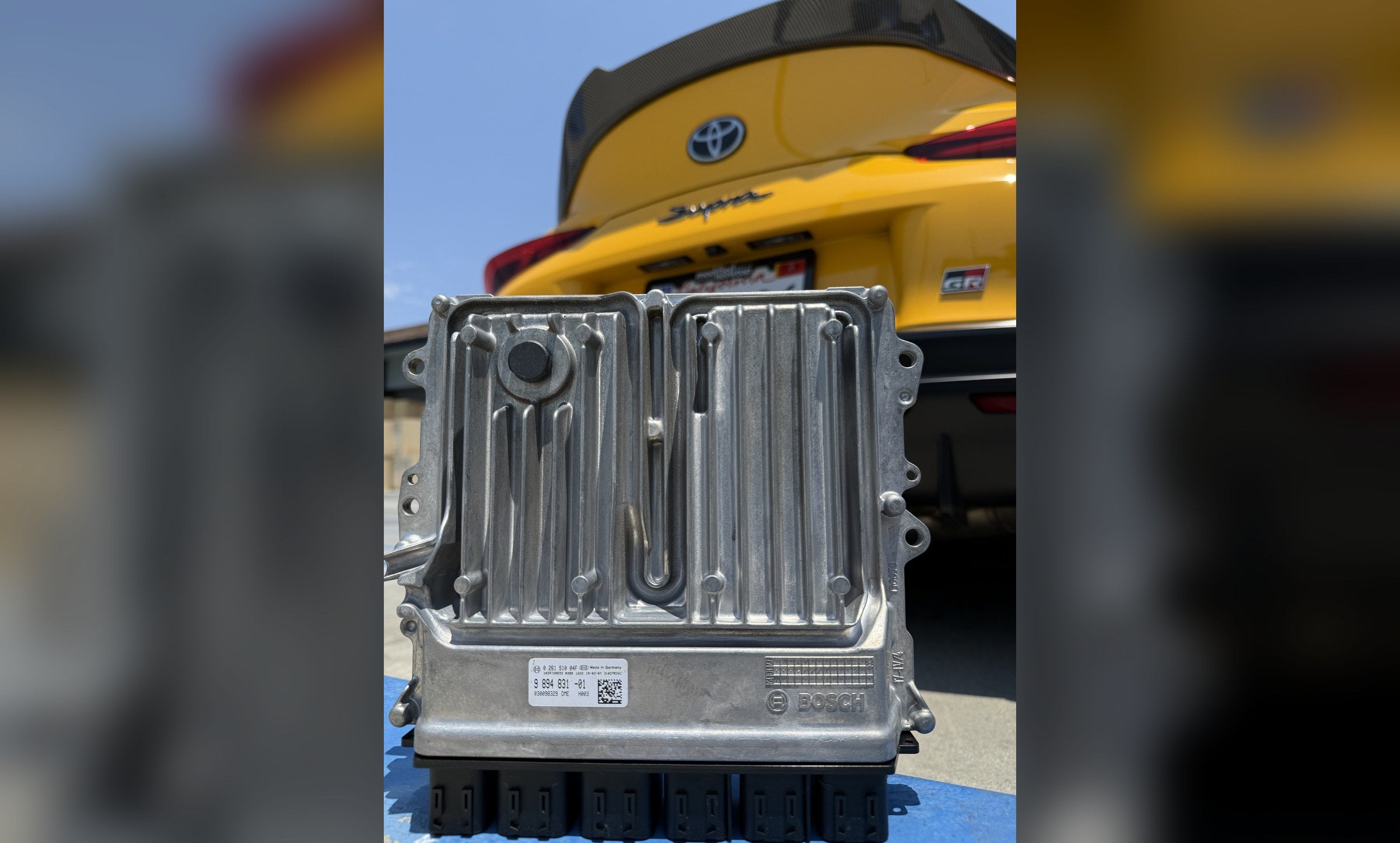 Bosch DME/ECU in front of a yellow Toyota GR Supra – Speed Logic services and repairs, Westminster CA
